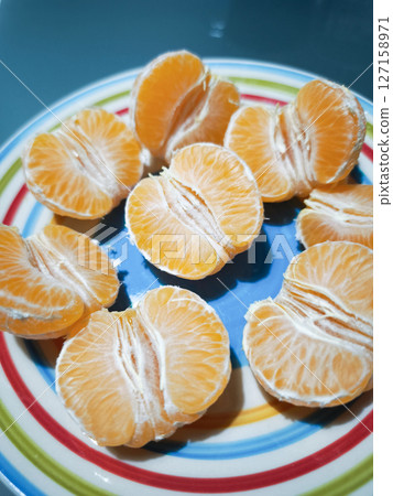 Juicy tangerine halves resting on multicolored plate, highlighting citrus texture and bright orange segments with fresh appeal Juicy tangerine halves resting on multicolored plate, highlighting citrus texture and bright orange segments with fresh appeal 127158971