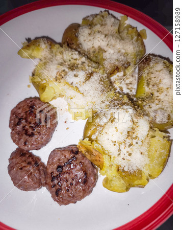 Rustic smashed potatoes generously sprinkled with melted cheese, herbed garnish, served alongside savory meatballs creating hearty autumn comfort 127158989