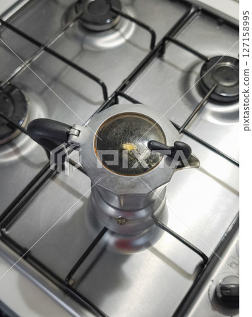 Moka pot rich espresso on stainless steel stovetop, traditional italian coffee ritual in rustic kitchen 127158995