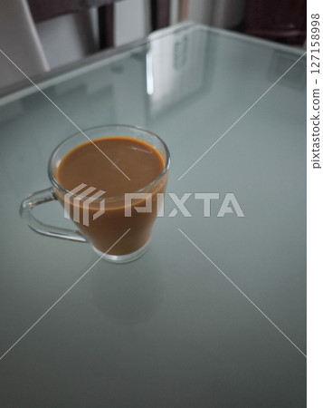 Steaming coffee mug resting on glass surface, reflecting warm ambiance of late autumn in aosta, italy Steaming coffee mug resting on glass surface, reflecting warm ambiance of late autumn in aosta, italy 127158998