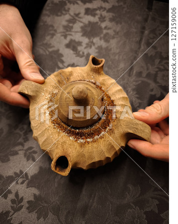Weathered hands cradling handcrafted wooden teapot on rustic linen, artisan woodworking detail from aosta valley, italy coffee in the grolla 127159006