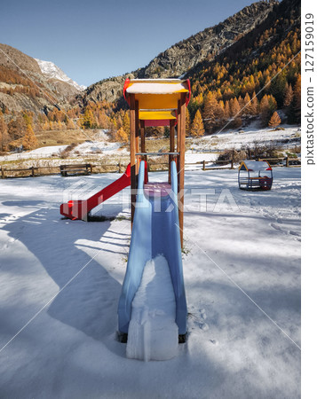 Snow covered playground slide nestled amid golden autumn landscape of aosta valley mountain scenery Frazionne Lillaz 127159019
