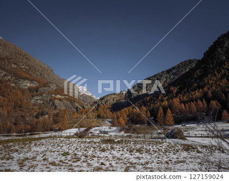Aosta valley landscape revealing snow kissed fields, golden autumn foliage, and towering alpine peaks under crisp winter approaching sky Frazionne Lillaz Aosta valley landscape revealing snow kissed fields, golden autumn foliage, and towering alpine peaks under crisp winter approaching sky Frazionne Lillaz 127159024