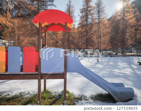 Vibrant playground standing against snow covered landscape and golden leaved trees in winter tinged aosta valley, italy Frazionne Lillaz 127159035