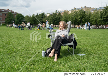 Woman sunbating in park. Glad female lounging in chair, resting napping with water bottle on break 127159374