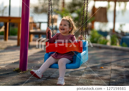 Portrait of a adorable little girl laughing when playing a swing Portrait of a adorable little girl laughing when playing a swing 127159381