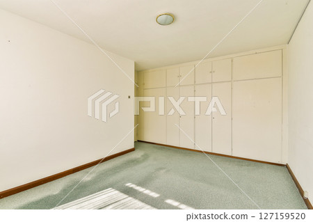 A spacious, minimalistic interior room featuring light-colored walls and a built-in wardrobe, illuminated by natural sunlight. A spacious, minimalistic interior room featuring light-colored walls and a built-in wardrobe, illuminated by natural sunlight. 127159520