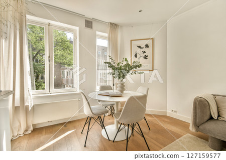 A stylish dining area featuring a round table surrounded by elegant chairs, large windows letting in natural light, and a touch of greenery. 127159577