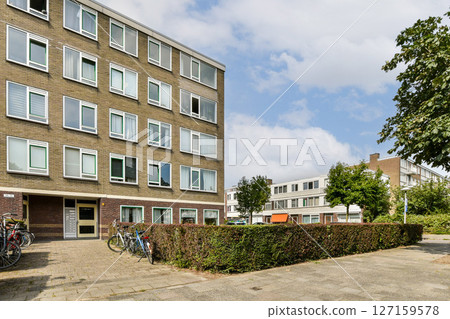 A contemporary building featuring large windows, surrounded by trees and manicured shrubs, with bicycles parked in front, showcasing urban living. 127159578