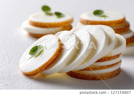 Mozzarella slices are artistically layered on a clean white surface, highlighting their smooth textures and delicate appearance. Concept of culinary arts, food photography, gourmet cheese 127159807