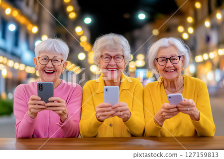 Three joyful older women engaged with their smartphones in a lively nighttime atmosphere adorned with fairy lights Three joyful older women engaged with their smartphones in a lively nighttime atmosphere adorned with fairy lights 127159813