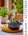 Lid of black pot lifted to reveal steaming mussels with fragrant vapors rising. Nearby, crispy shoestring fries blur in foreground. Concept of dining, culinary arts, seafood restaurant 127159820