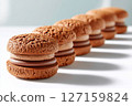 Chocolate sandwich cookies arranged in straight line on bright surface. Clean white background enhances the texture and appeal. Concept of dessert, bakery, snack food 127159824