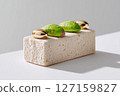 Dessert placed on clean white surface with shiny golden decorations and vibrant green toppings. Minimalist setting showcases modern food presentation 127159827