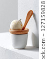 Creamy ice cream placed in a stylish white bowl with a wooden spoon. Minimalist setting with textured white surfaces creates modern aesthetic 127159828