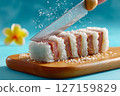 Hand slices Hawaiian spam musubi sushi roll on wooden board showcasing sticky rice and color contrast. Tropical surfboards enhance the beach vibe 127159829