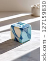 Marbled blue and white cheese cube placed centrally on clean white background. Soft natural light creates gentle shadows in modern minimalist setting 127159830