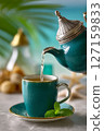 Ceremonial pour of Moroccan mint tea from silver teapot creates emerald waterfall effect. Bright, tropical background enhances vibrant ambiance 127159833