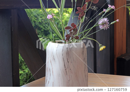 Marble vase with wildflowers on table. Terrace in summer. Design and wooden furniture. Marble vase with wildflowers on table. Terrace in summer. Design and wooden furniture. 127160759