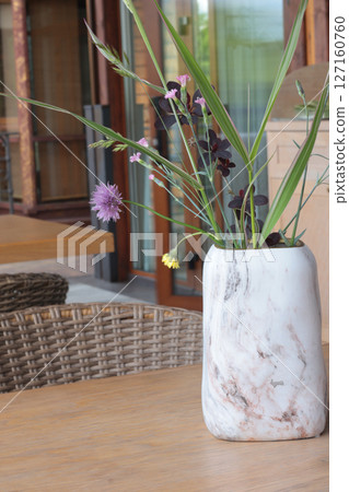 Marble vase with wildflowers on table. Terrace in summer. Design and wooden wicker furniture. Marble vase with wildflowers on table. Terrace in summer. Design and wooden wicker furniture. 127160760