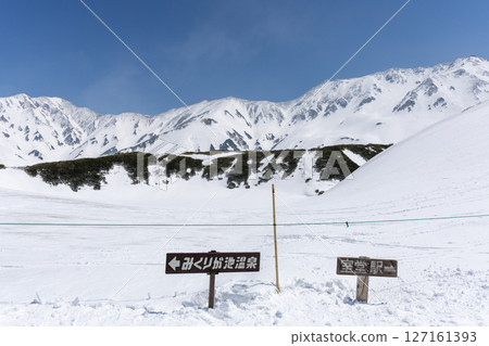 A snowy trail sign pointing to Murodo Station and Mikurigaike Onsen on a sunny day in Tateyama 127161393