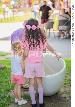 Girls wearing pink flower crowns and colorful outfits enjoying festival outdoors on sunny day. annual Kazanlak rosa damascene Festival. Concept of childhood joy, festive spirit Girls wearing pink flower crowns and colorful outfits enjoying festival outdoors on sunny day. annual Kazanlak rosa damascene Festival. Concept of childhood joy, festive spirit 127161580