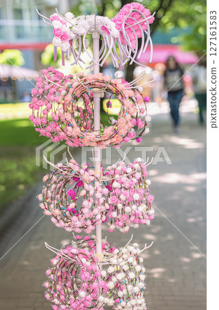 Colorful flower headbands with mini roses in shades of pink and white displayed on street market stand. Traditional cultural Rose festival. Concept of romantic accessory, festive charm Colorful flower headbands with mini roses in shades of pink and white displayed on street market stand. Traditional cultural Rose festival. Concept of romantic accessory, festive charm 127161583