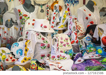 Painted fashion items with vibrant floral designs displayed on market stand in artistic composition. Concept of wearable art, custom design, creative expression 127161586
