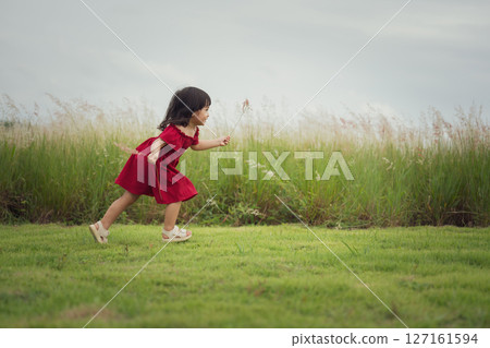 happy toddle girl in red dress running on grass field 127161594