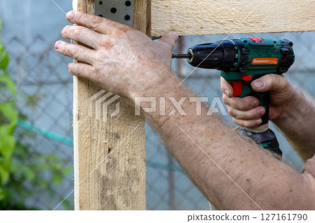 Close-up of men's hands using drill to assemble wooden structure 127161790