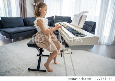 Little girl playing piano at home in the living room. Childhood creativity and musical development in cozy family environment 127161958