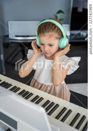 Little girl practicing piano with wireless headphones at home. Early childhood development through modern and focused music education. 127161969