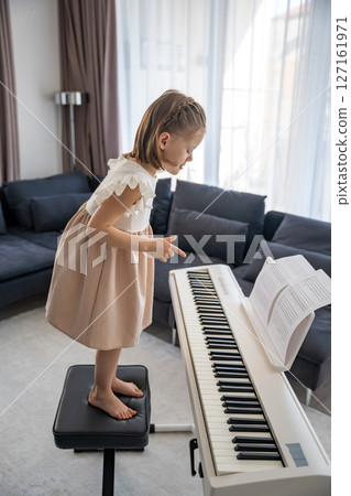 Little girl refusing to play piano during home music lesson. Playful resistance and emotional expression in early childhood learning process. 127161971