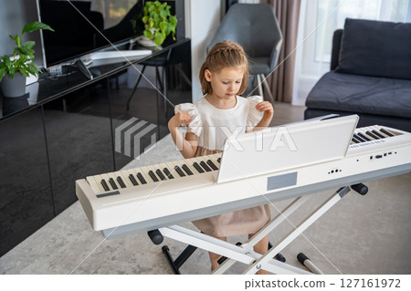 Little girl preparing to play piano at home in the living room. Calm moment of focus and anticipation before music practice in a cozy family space. 127161972