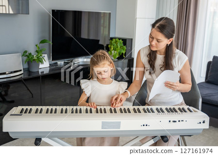 Individual piano lesson for a young child at home in the living room. Concept of early childhood development through personalized music education. 127161974