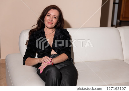 brunette woman in dark clothes sitting on white sofa in living room interior brunette woman in dark clothes sitting on white sofa in living room interior 127162107