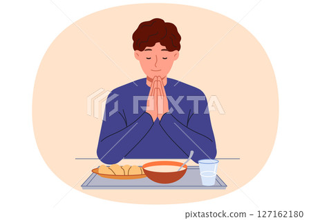 Man prays sitting at table with food, observing christian tradition and expressing gratitude to god 127162180