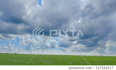 A vast and expansive landscape showcases a dramatic cloudscape hovering over a lush green field 127162617