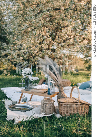 Elegant picnic setup under blooming trees in a serene outdoor location during springtime Elegant picnic setup under blooming trees in a serene outdoor location during springtime 127162880