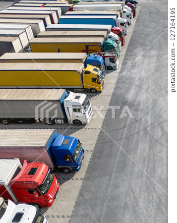 Aerial view of a large truck parking lot at a logistics hub, with multiple commercial semi trucks parked in organized rows 127164195