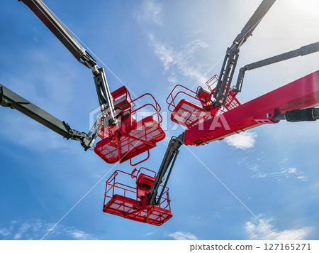 Workers operating lift equipment under clear blue sky during outdoor construction activity near urban area 127165271