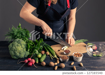 Woman chopping cheese tofu with fresh vegetables and nuts on table. Woman chopping cheese tofu with fresh vegetables and nuts on table. 127165540
