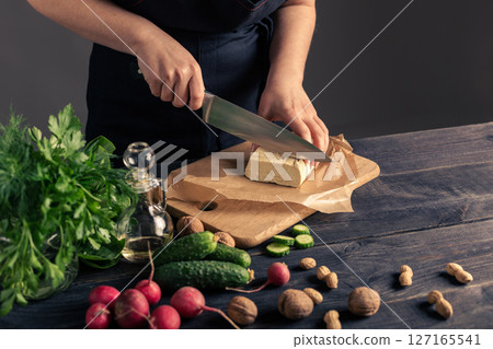 Woman chopping tofu with fresh vegetables and nuts on table Woman chopping tofu with fresh vegetables and nuts on table 127165541