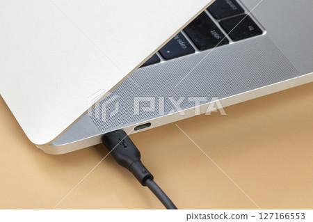 cable plugged in laptop on beige background, close-up. Charging battery laptop 127166553