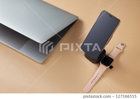 Laptop with smart watch and smartphone charging on wireless charger on beige table, Modern workplace device Laptop with smart watch and smartphone charging on wireless charger on beige table, Modern workplace device 127166555