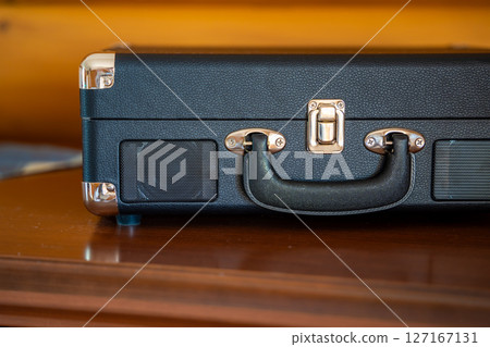 Closed vintage-style record player in suitcase design on wooden table. Retro audio equipment ready to play vinyl in cozy home setting 127167131