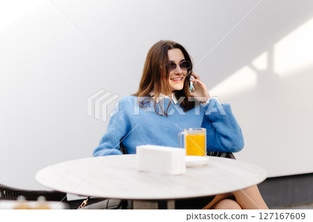 Young woman talking on smartphone and drinking orange juice at outdoor cafe Young woman talking on smartphone and drinking orange juice at outdoor cafe 127167609