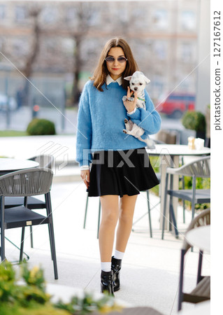 Stylish woman holding small dog walking in urban city Stylish woman holding small dog walking in urban city 127167612