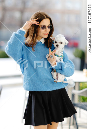 Stylish woman holding small dog walking in urban city 127167613