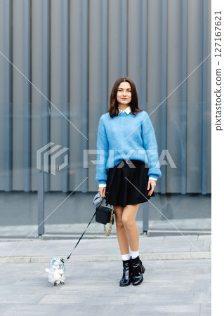 Young woman walking her dog in the city wearing a blue sweater and black skirt Young woman walking her dog in the city wearing a blue sweater and black skirt 127167621